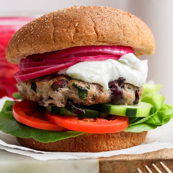 A greek turkey burger on a whole wheat bun with lettuce, tomato, cucumber, tzatziki and pickled onions.