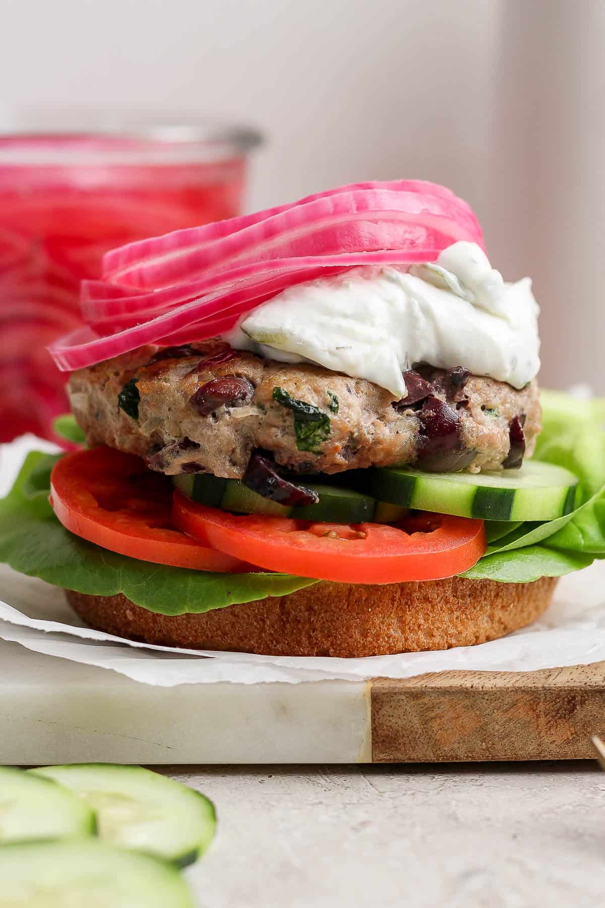 A fully topped greek turkey burger on a bottom bun.