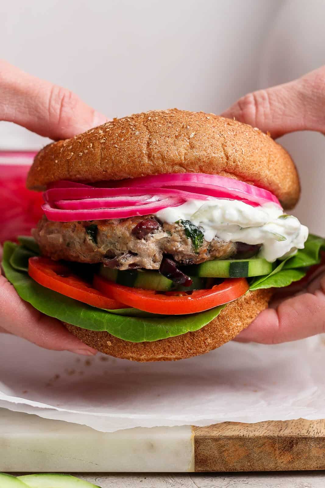 Hands holding a greek turkey buger with tzatziki sauce.