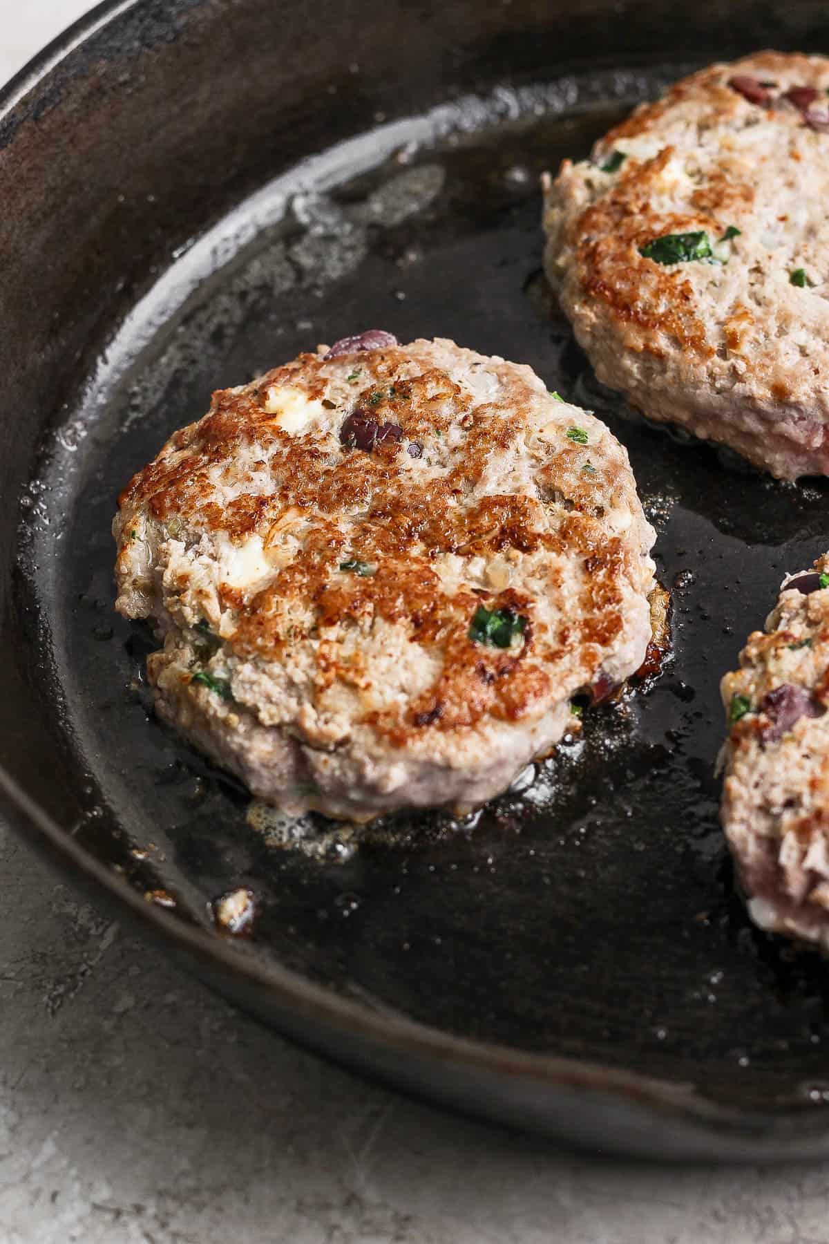 Greek turkey burgers searing on a cast iron skillet.