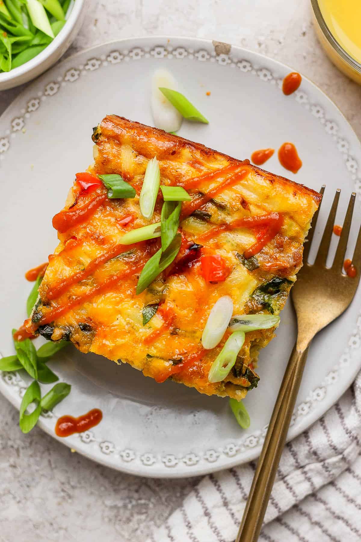 A square of the egg bake on a plate topped with hot sauce and sliced green onions.