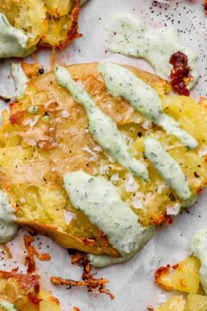 A smashed potato on piece of parchment with herby green sauce drizzled over top.