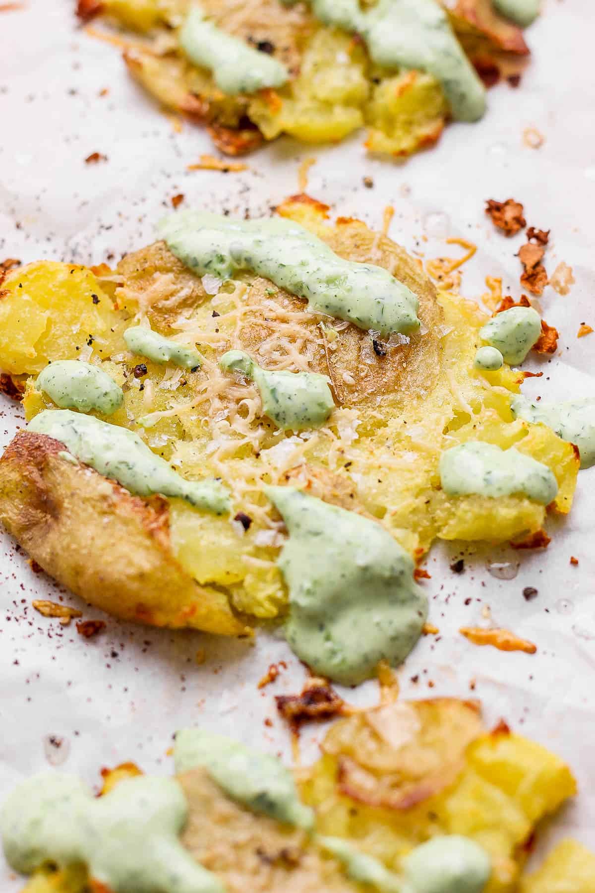 Smashed potatoes with green sauce on a sheet pan.