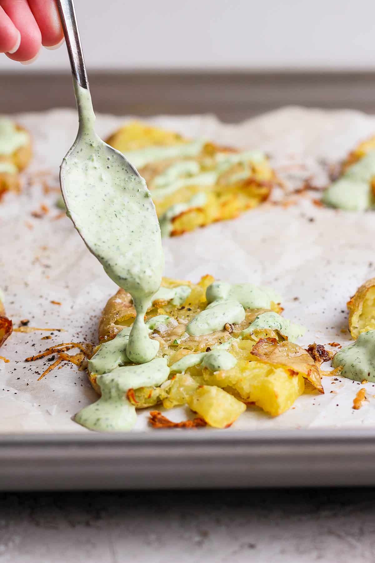 Green sauce being drizzled on the smashed potatoes.