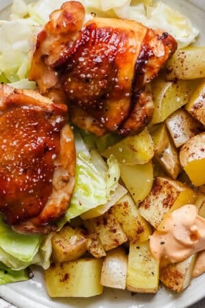 A plate filled with sheet pan chicken and cabbage with potatoes and gochujang mayo.