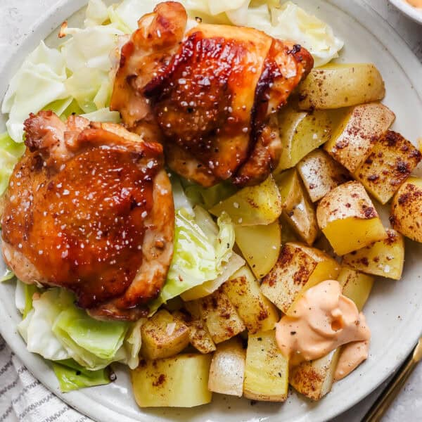 A plate filled with sheet pan chicken and cabbage with potatoes and gochujang mayo.