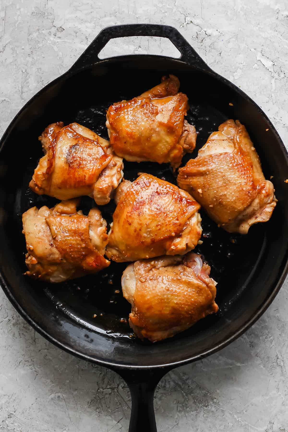 Marinated chicken thighs searing in a cast iron skillet.