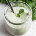 A small jar of homemade avocado lime ranch dressing with a little cilantro on top and spoon sticking out.