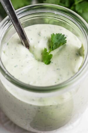 A small jar of homemade avocado lime ranch dressing with a little cilantro on top and spoon sticking out.