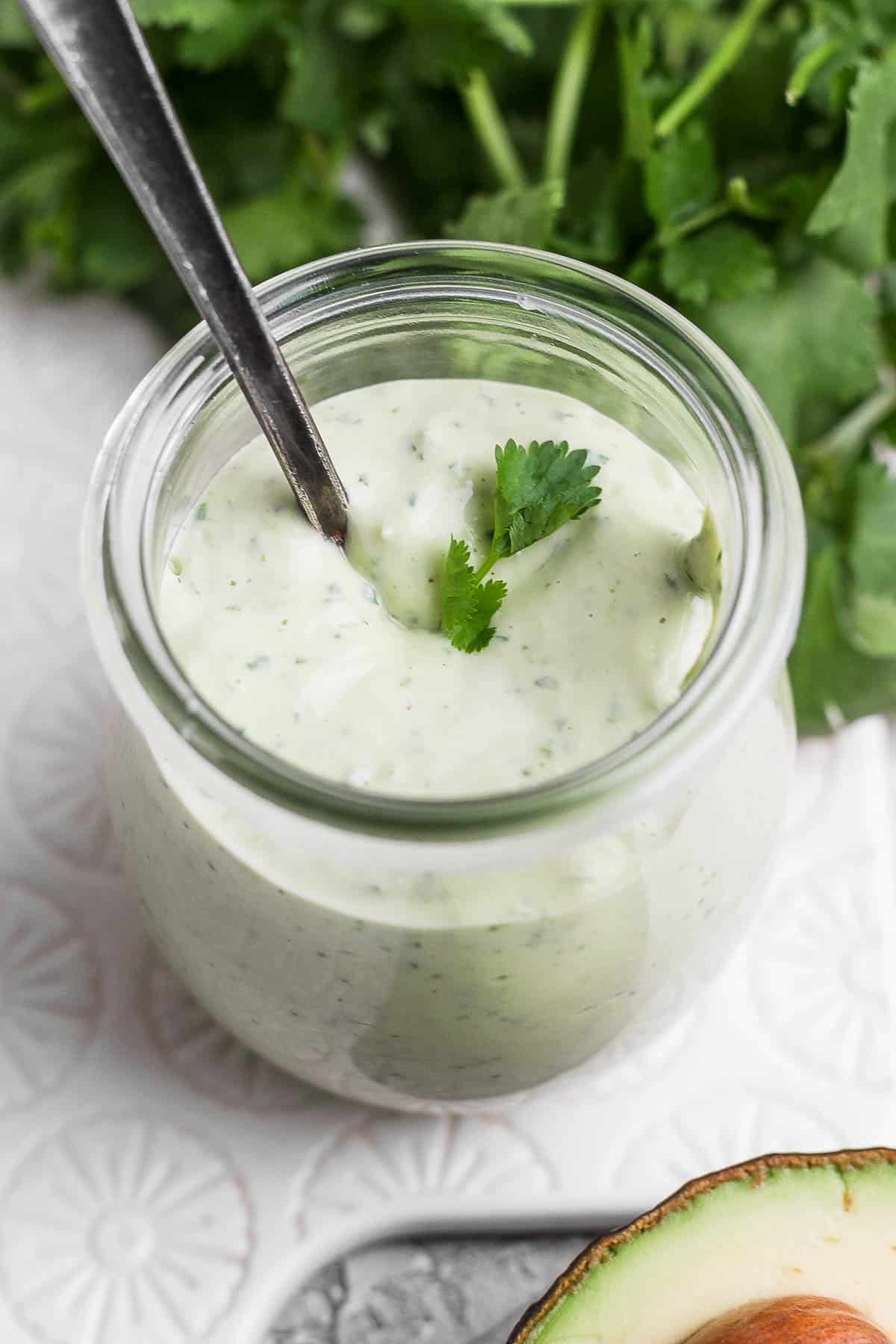 A glass jar of avocado lime ranch dressing with a garnish of cilantro leaves on the top.