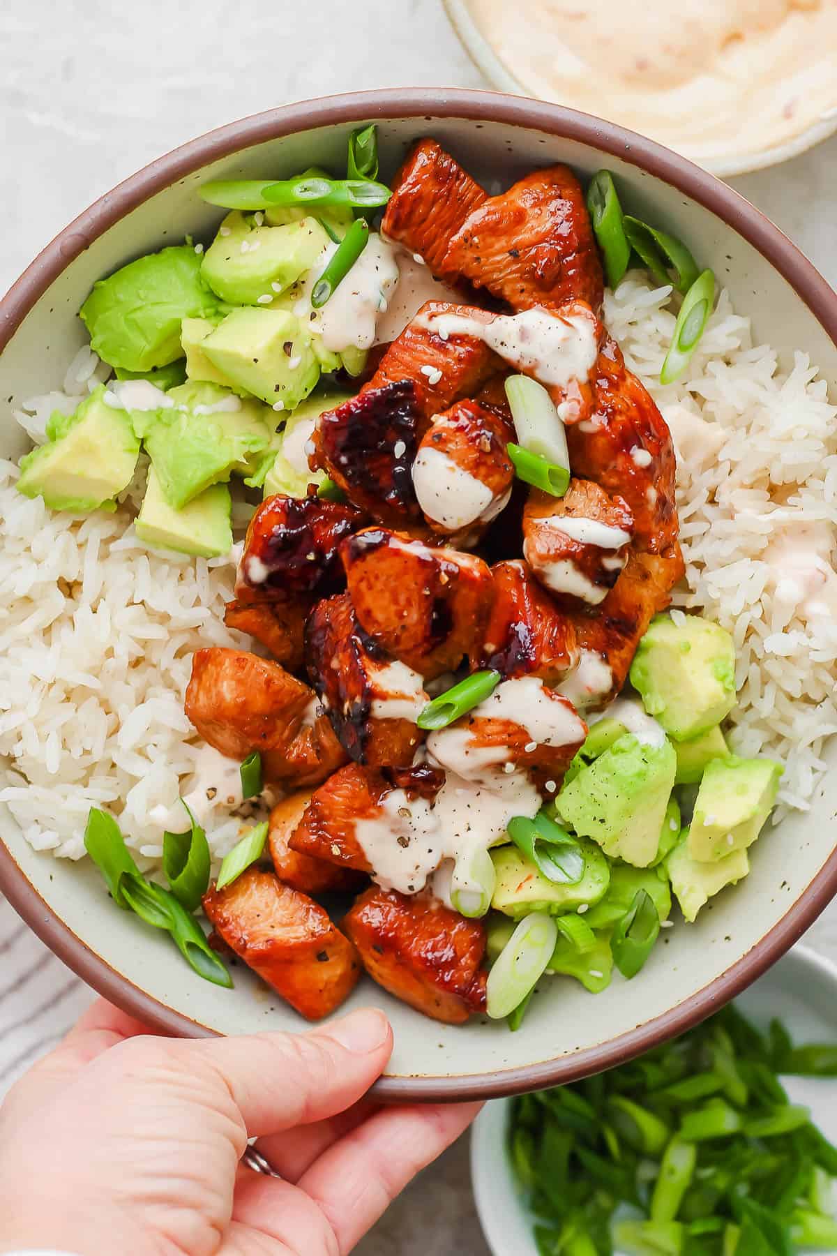 Bang Bang chicken over a bed of rice garnished with avocado, green onion, and bang bang sauce.