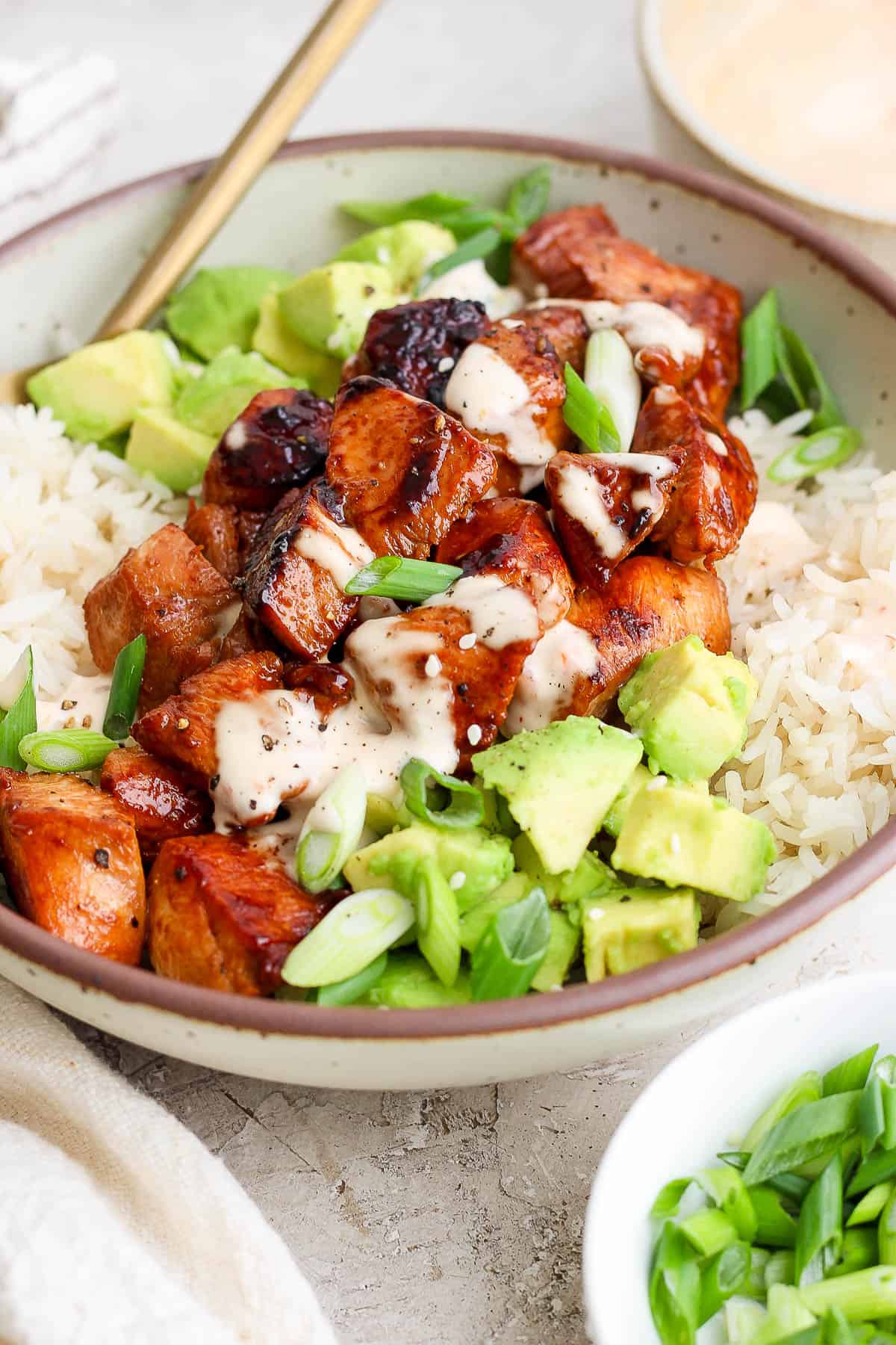 Bang Bang chicken over a bed or rice surrounded by cubed avocado and sliced green onions.