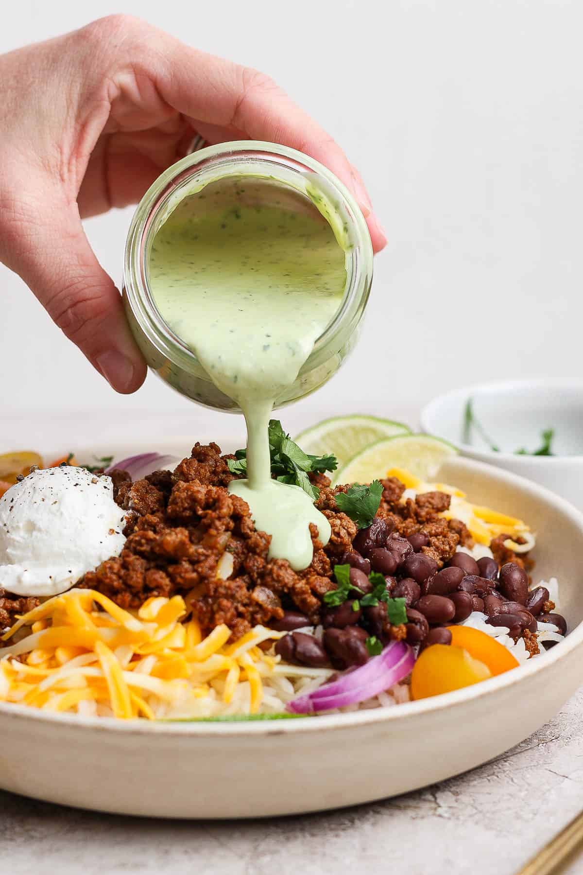 A ground beef taco rice bowl being poured with cilantro lime ranch dressing.