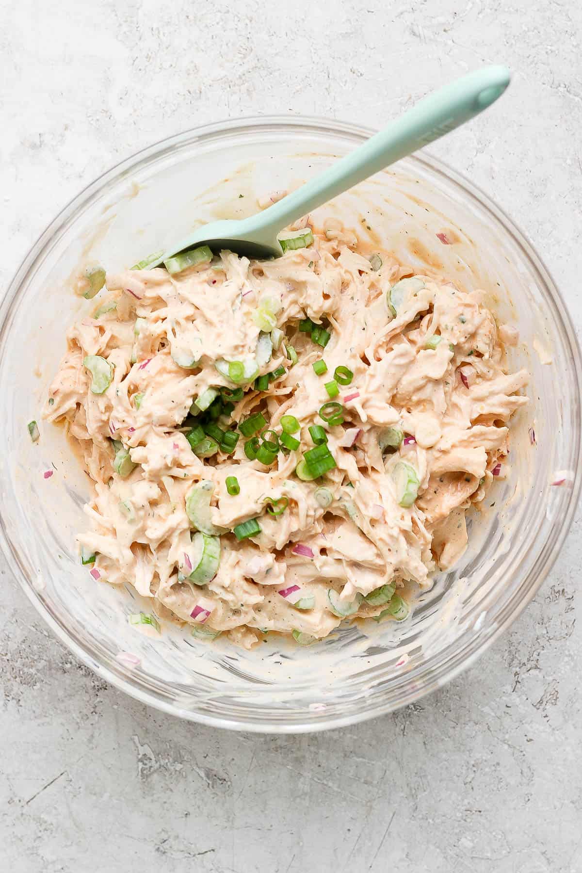 Buffalo ranch chicken salad ingredients mixed together in a glass bowl.