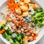 A buffalo chicken rice bowl with celery, cucumber, roasted cauliflower, carrots, blue cheese and chicken.