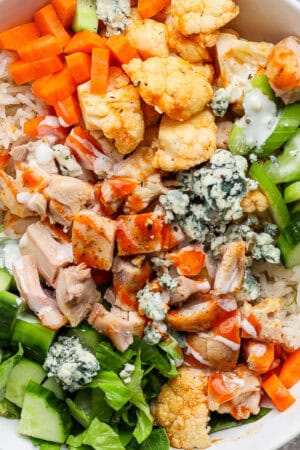 A buffalo chicken rice bowl with celery, cucumber, roasted cauliflower, carrots, blue cheese and chicken.