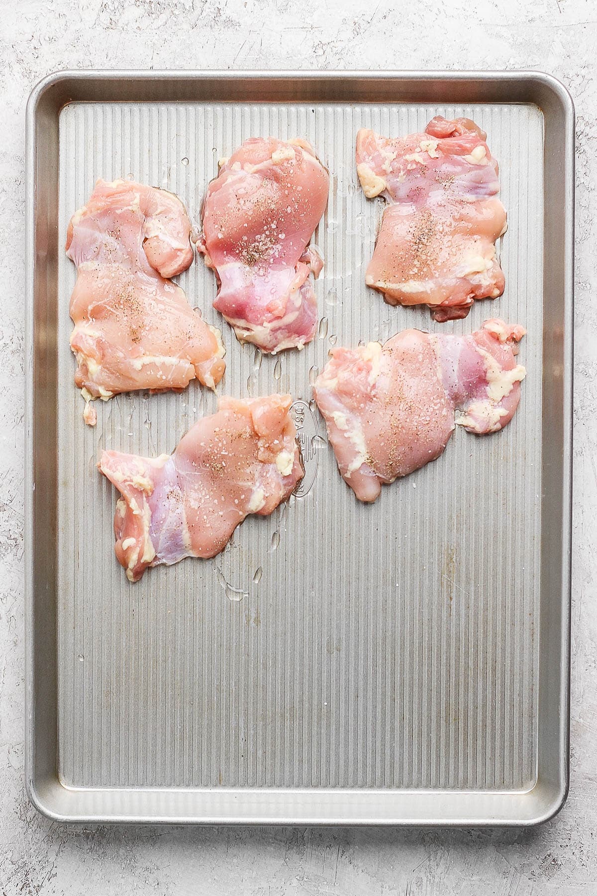 Five seasoned chicken thighs on one half of a baking sheet to make a buffalo chicken rice bowl.