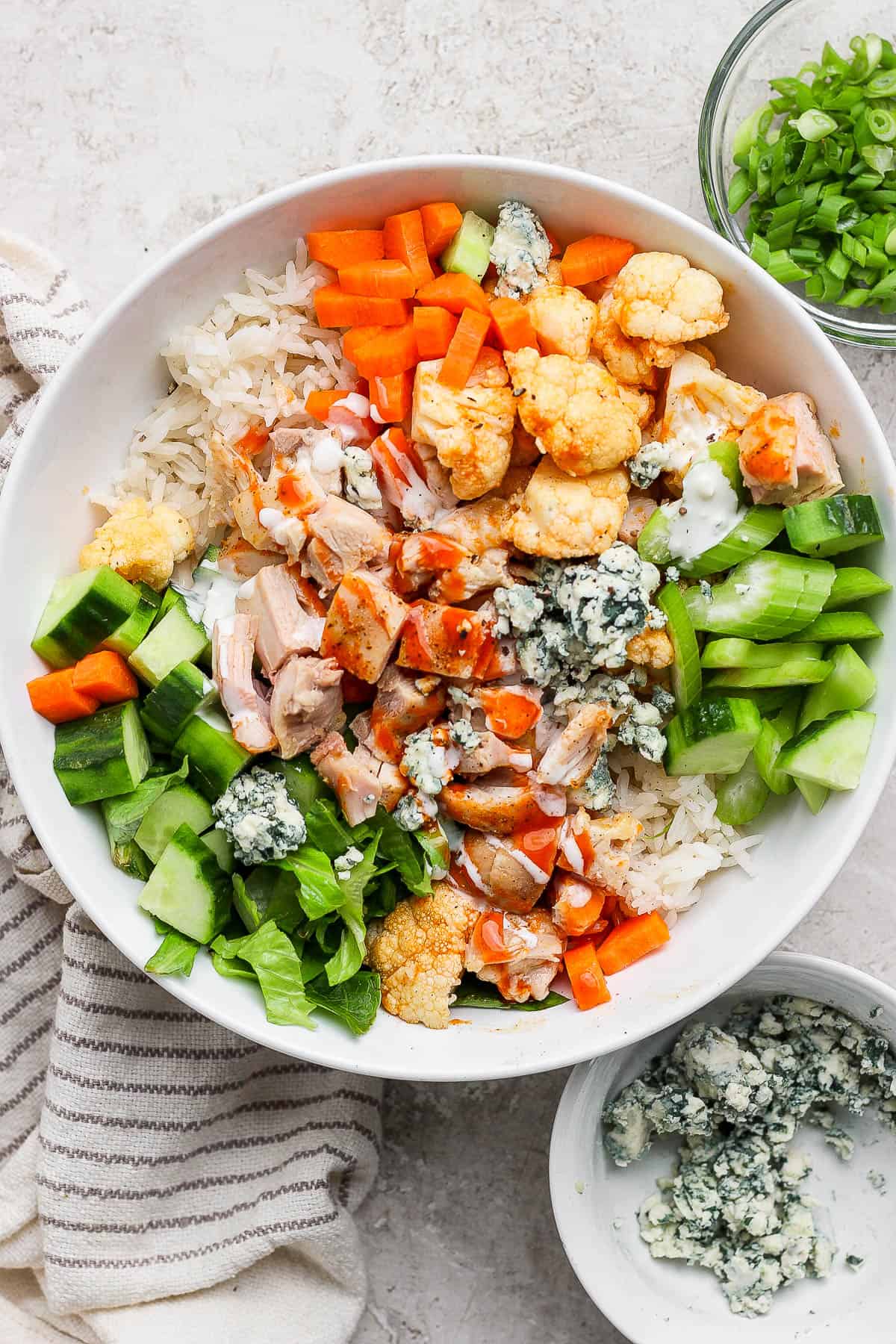 A bowl with rice, carrots, cucumber, celery, blue cheese, cubed chicken and buffalo sauce and ranch.