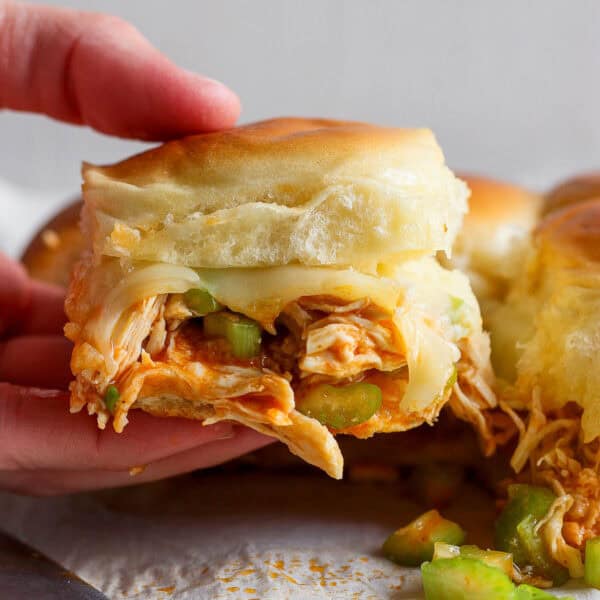 Someone holding a buffalo chicken slider with melted cheese and green onions.