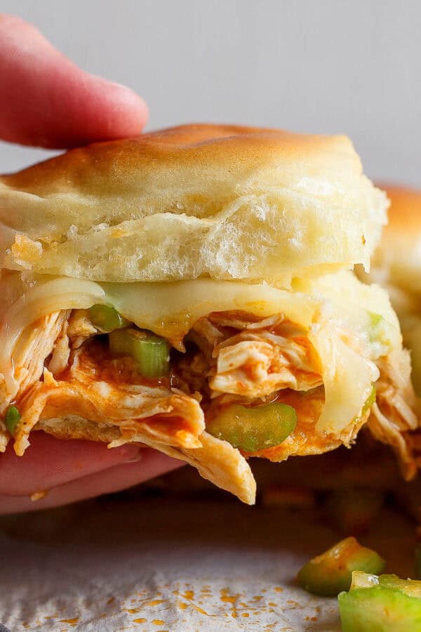Someone holding a buffalo chicken slider with melted cheese and green onions.
