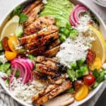 A Chicken Shawarma Bowl filled with cooked chicken, pickled red onions, tomatoes, lemon, avocado, feta cheese and garlic white sauce.