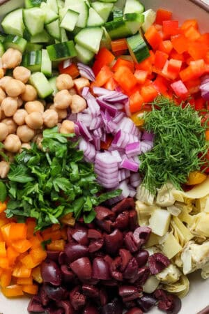 Top down shot of a large bowl filled with a mediterranean chickpea salad with cucumber, bell peppers, onion, olives and artichoke hearts.