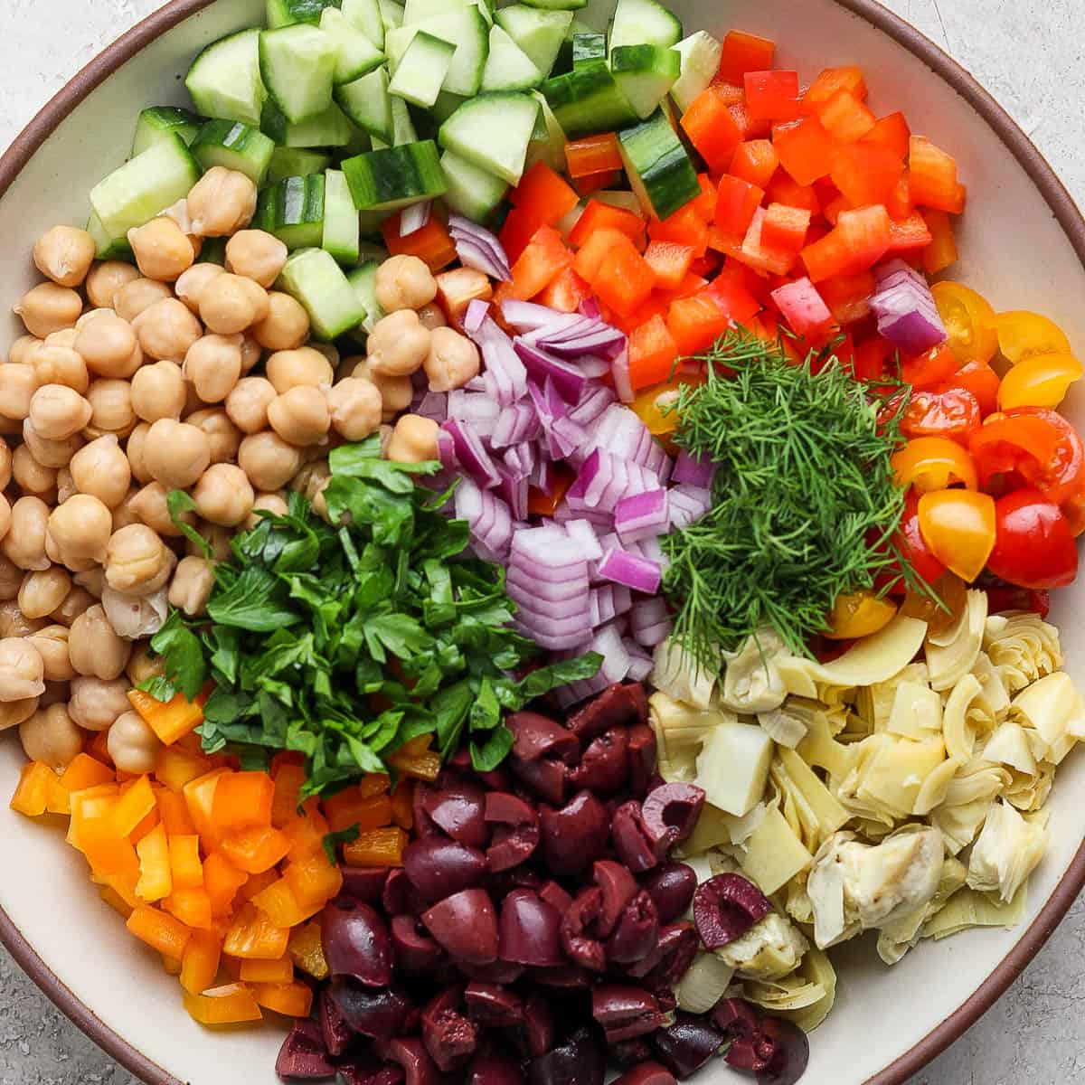 Top down shot of a large bowl filled with a mediterranean chickpea salad with cucumber, bell peppers, onion, olives and artichoke hearts.