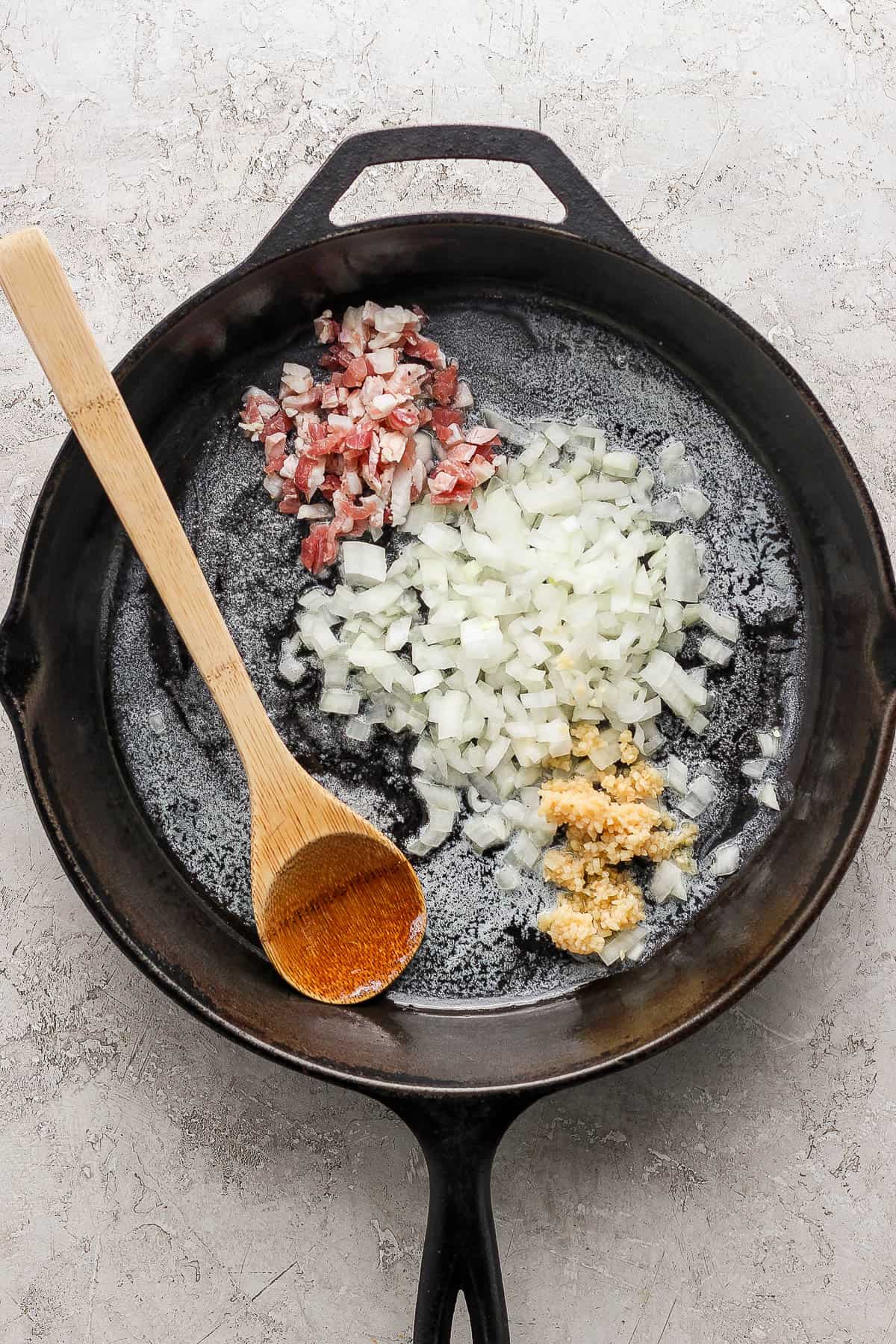 Melted butter, pancetta, onion, and garlic in the cast iron skillet with a wooden spoon.