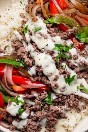 A philly cheesesteak rice bowl with ground beef, rice, cheese sauce and cooked onions and bell peppers.