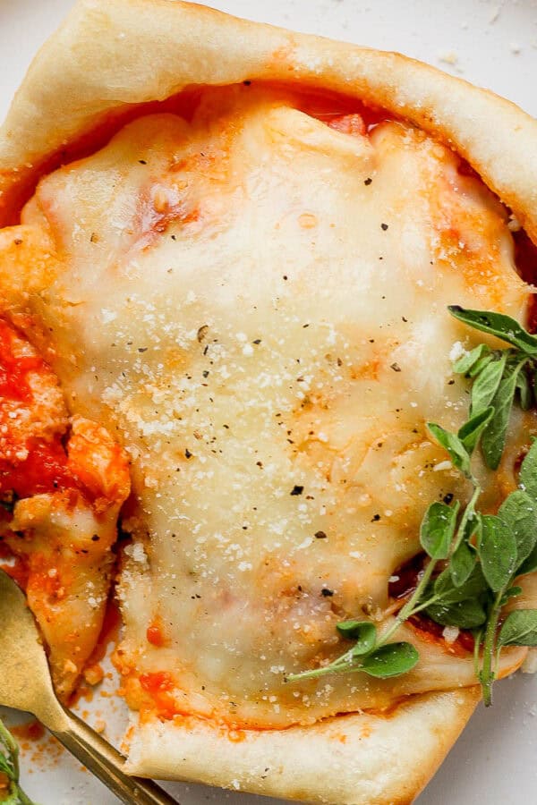 A pizza pot pie on a plate with a gold fork on the side and fresh oregano garnish.