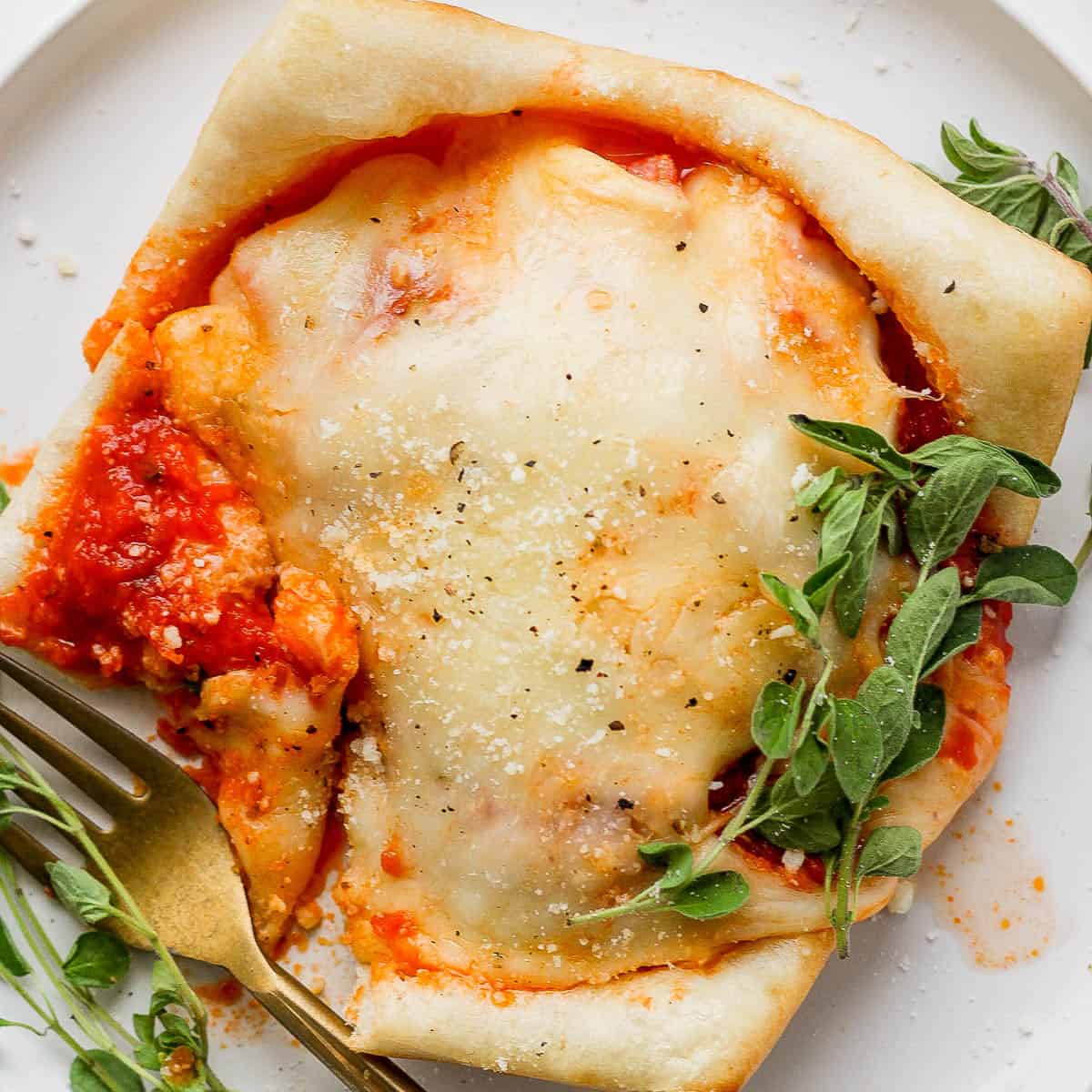 A pizza pot pie on a plate with a gold fork on the side and fresh oregano garnish.