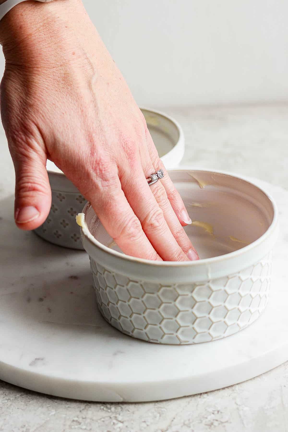 A hand rubbing butter in a ramekin.