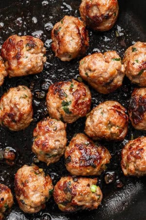 Close up shot of a cast iron skillet filled with cooked pork meatballs.