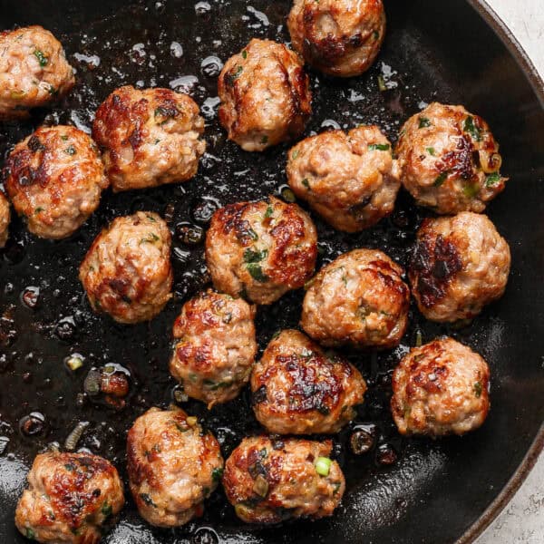 Close up shot of a cast iron skillet filled with cooked pork meatballs.