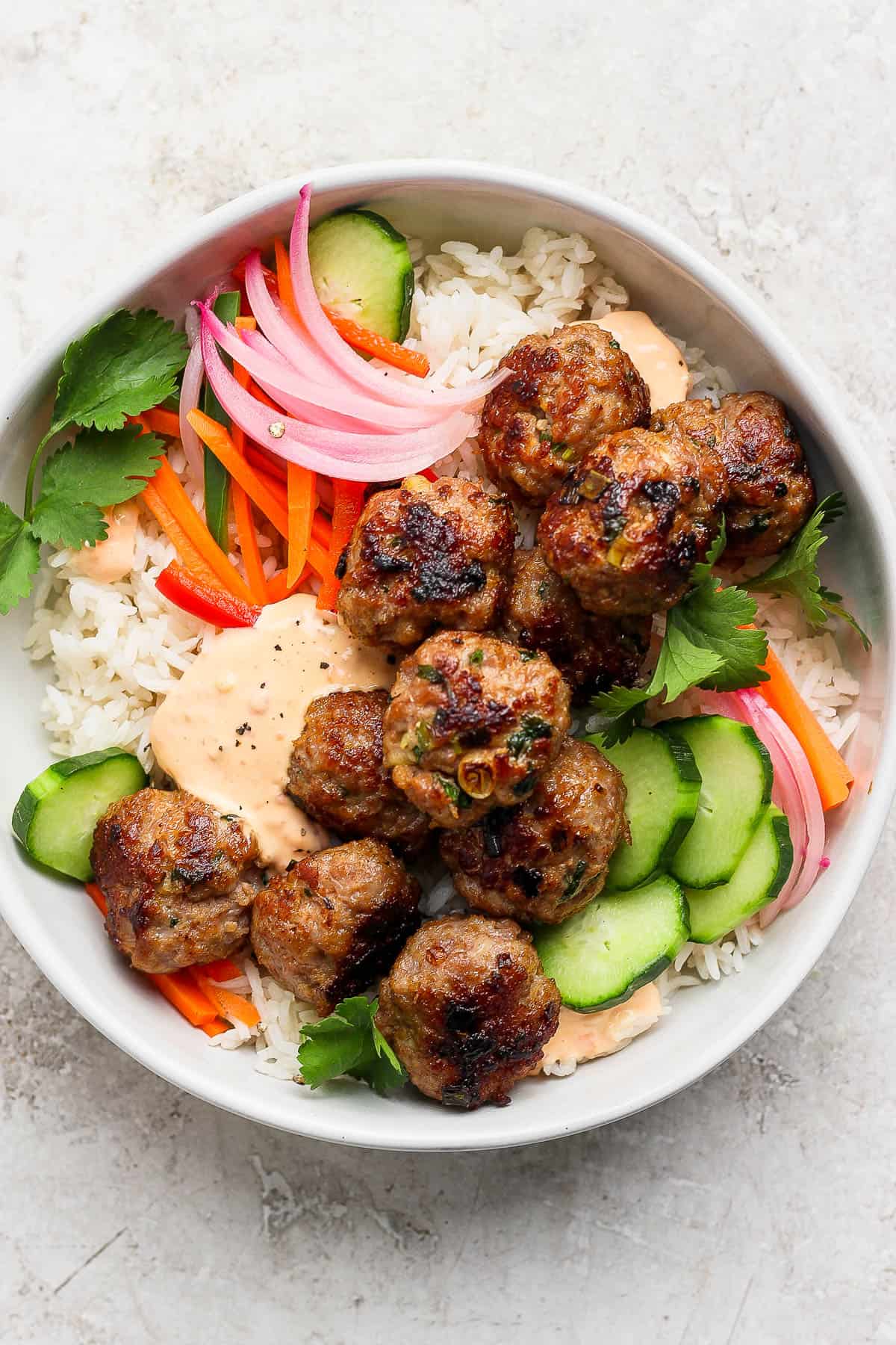 Pork meatballs in a bowl with rice, pickled vegetables, sauce, and cilantro. 