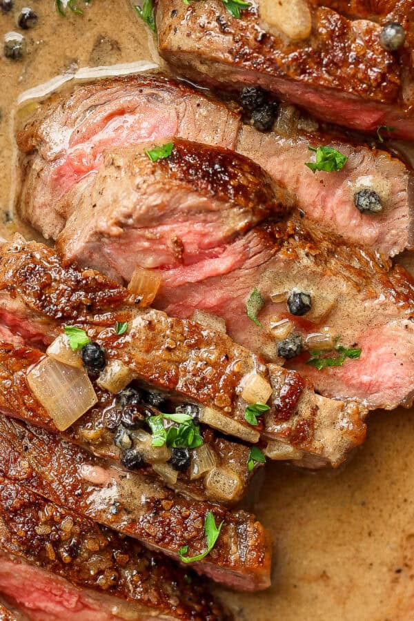 Sliced steak au poivre in a cast iron skillet.