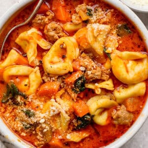 A bowl of cheese tortellini soup with a spoon sticking out and crumbled parmesan cheese.