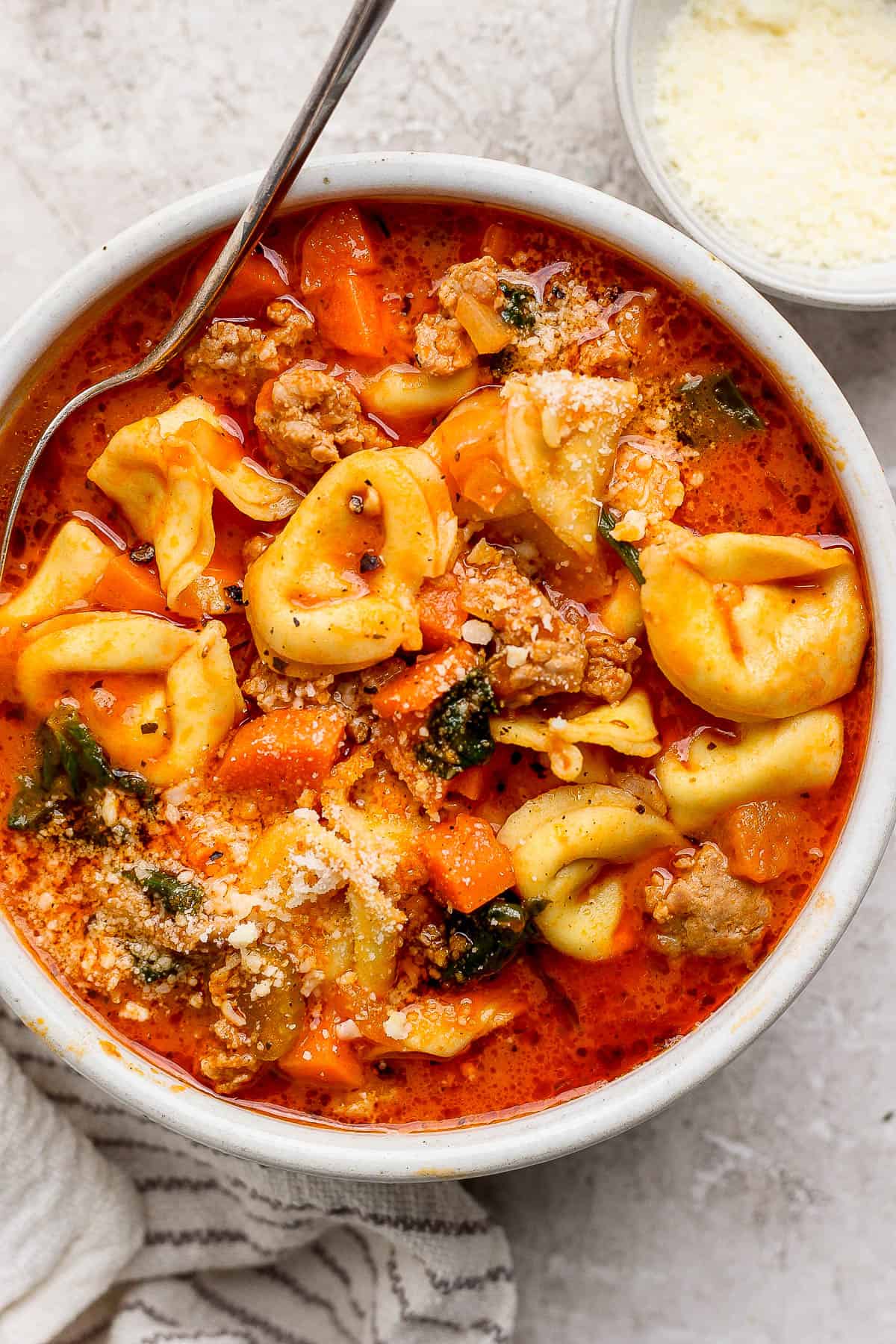 A bowl of tortellini soup with parmesan cheese on top.