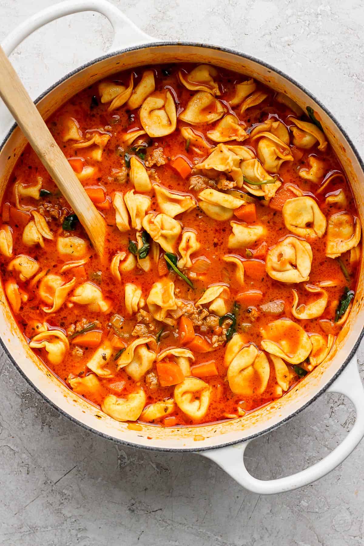 The complete tortellini soup in a pot with a wooden spoon.