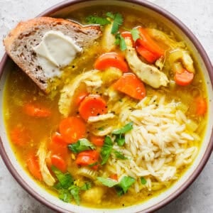 Bowl of Turmeric Chicken Soup with a piece of bread with butter sticking out.