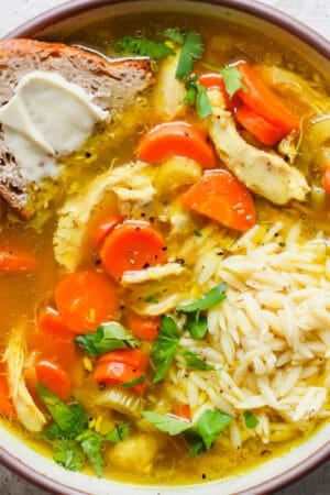 Bowl of Turmeric Chicken Soup with a piece of bread with butter sticking out.