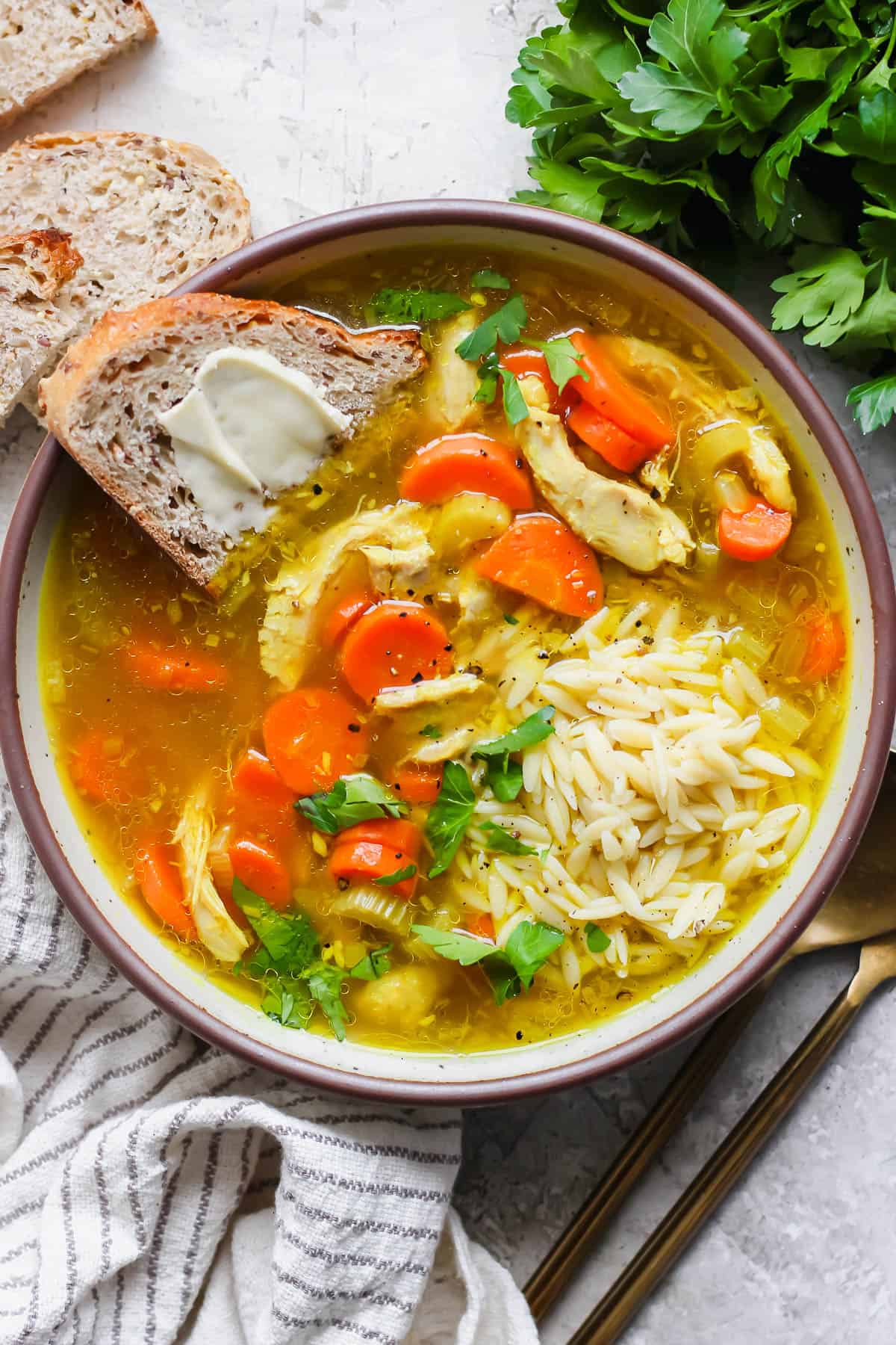 A bowl of turmeric chicken soup with a slice of buttered bread.