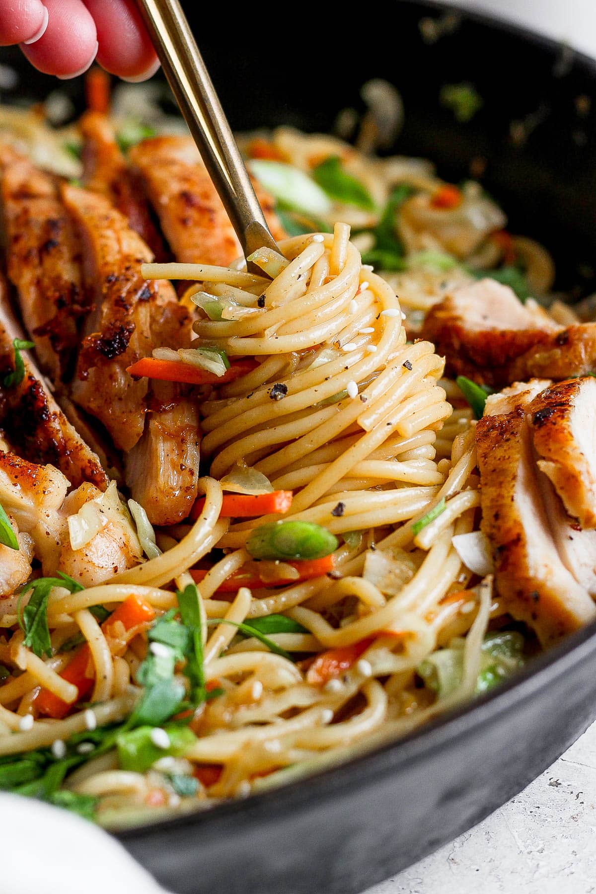 A hand holding a fork and twirling chicken chow mein noodles around the fork.