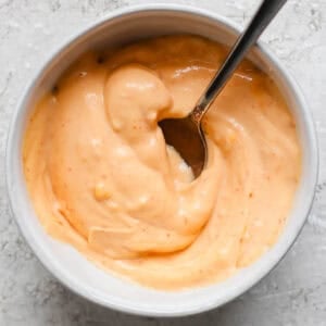 A bowl of gochujang mayo with a spoon sticking out.