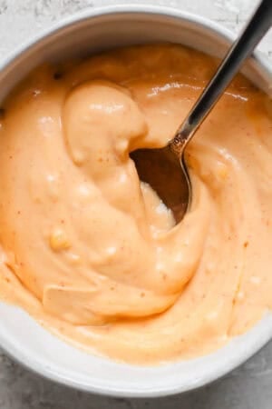 A bowl of gochujang mayo with a spoon sticking out.