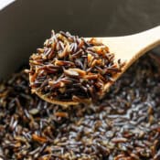A wooden spoon filled with cooked wild rice over a pot filled with more cooked wild rice.