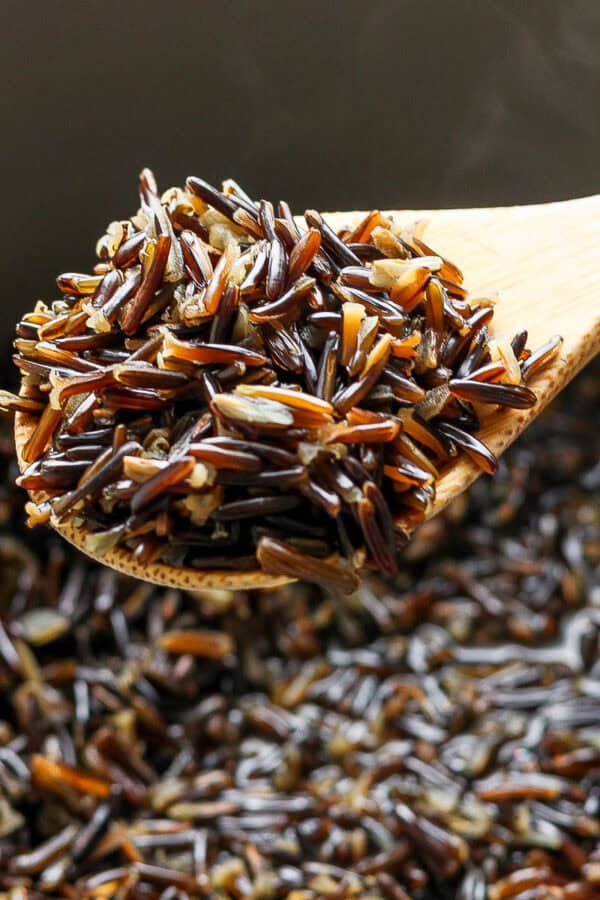 A wooden spoon filled with cooked wild rice over a pot filled with more cooked wild rice.
