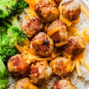 A plate with rice, broccoli and turkey cheddar meatballs with shredded cheddar cheese around the meatballs.