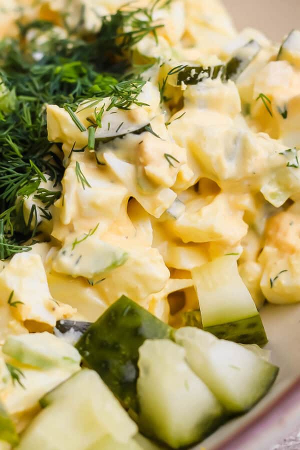 Close up shot of some dil pickle egg salad in a bowl with dill and cut up pickles.