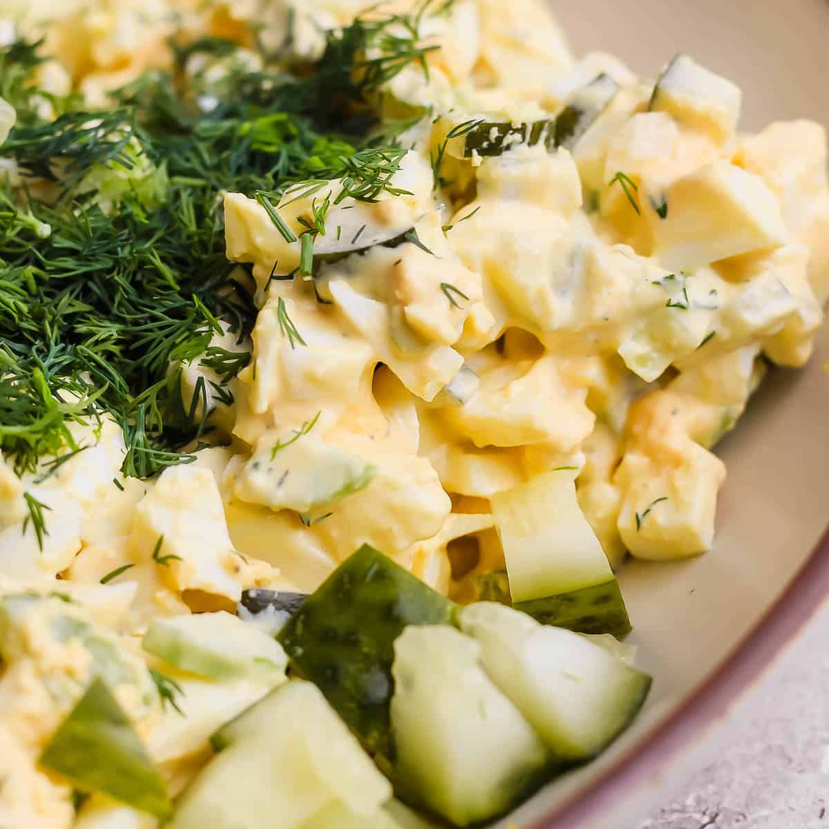 Close up shot of some dil pickle egg salad in a bowl with dill and cut up pickles.